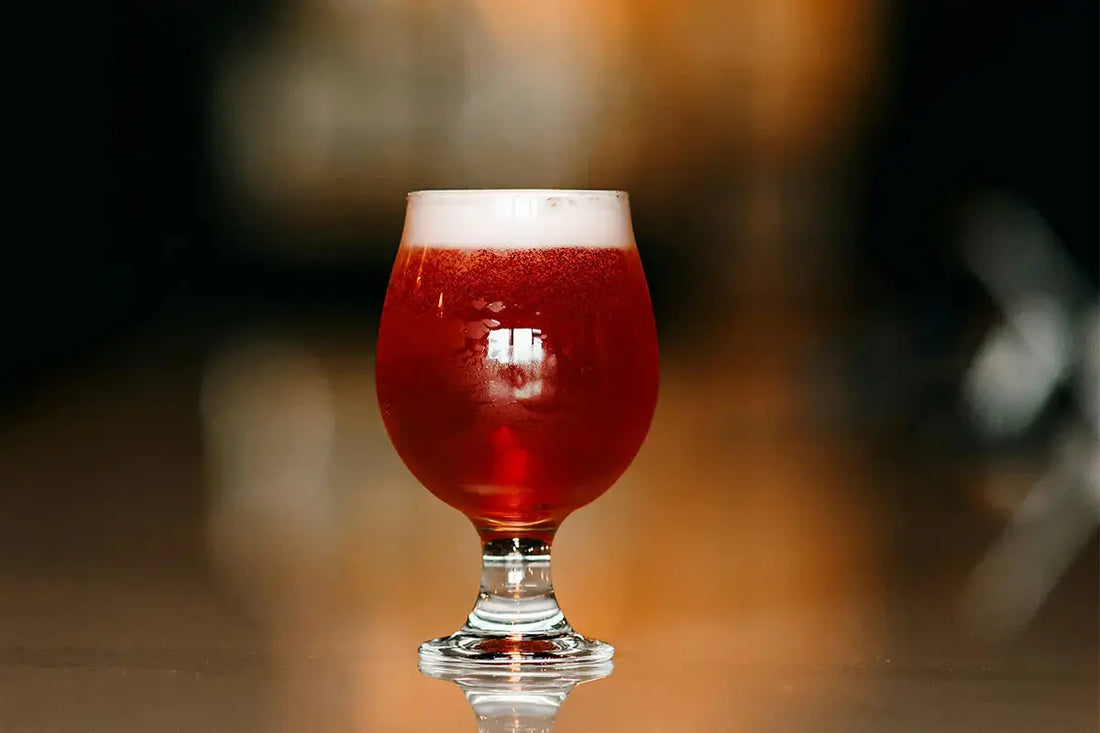 Bière gose aux fruits rouges dans un verre de bière à pied. Le verre est seul sur une table de bar.