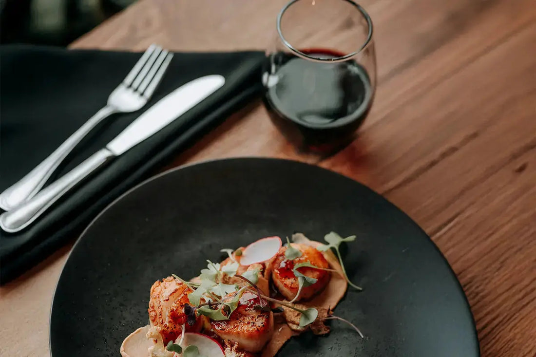 Plat de Saint-Jacques avec un verre de vin rouge sans pied à côté.