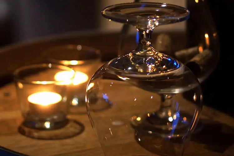 Verres à cognac élégamment retournés sur un plateau, reflétant la lueur douce de bougies allumées, créant une ambiance chaleureuse et raffinée.