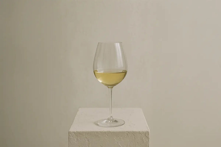 Verre à vin blanc posé sur un socle texturé en pierre claire, dans un décor minimaliste et chaleureux, éclairé par une lumière douce.
