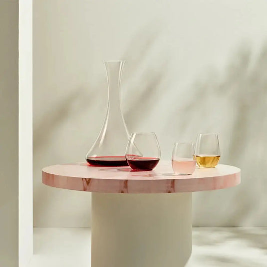 Carafe à vin Jazz en verre soufflé, présentée sur une table ronde rose avec trois verres de dégustation aux couleurs variées.