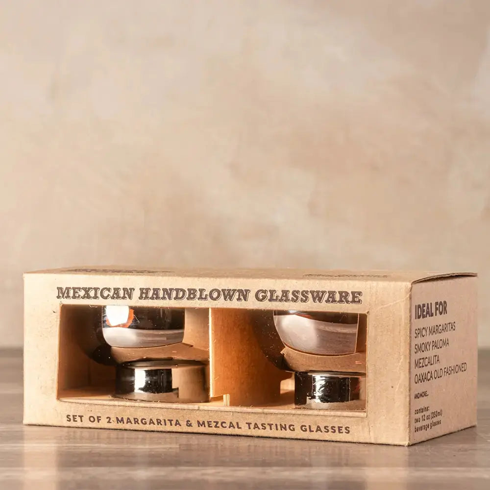 Emballage en carton naturel contenant un set de deux verres soufflés à la main pour la dégustation de mezcal et de margaritas. L’emballage affiche l’inscription 'Mexican Handblown Glassware' et mentionne les cocktails idéaux pour ces verres, tels que Spicy Margarita, Smoky Paloma et Mezcalita.