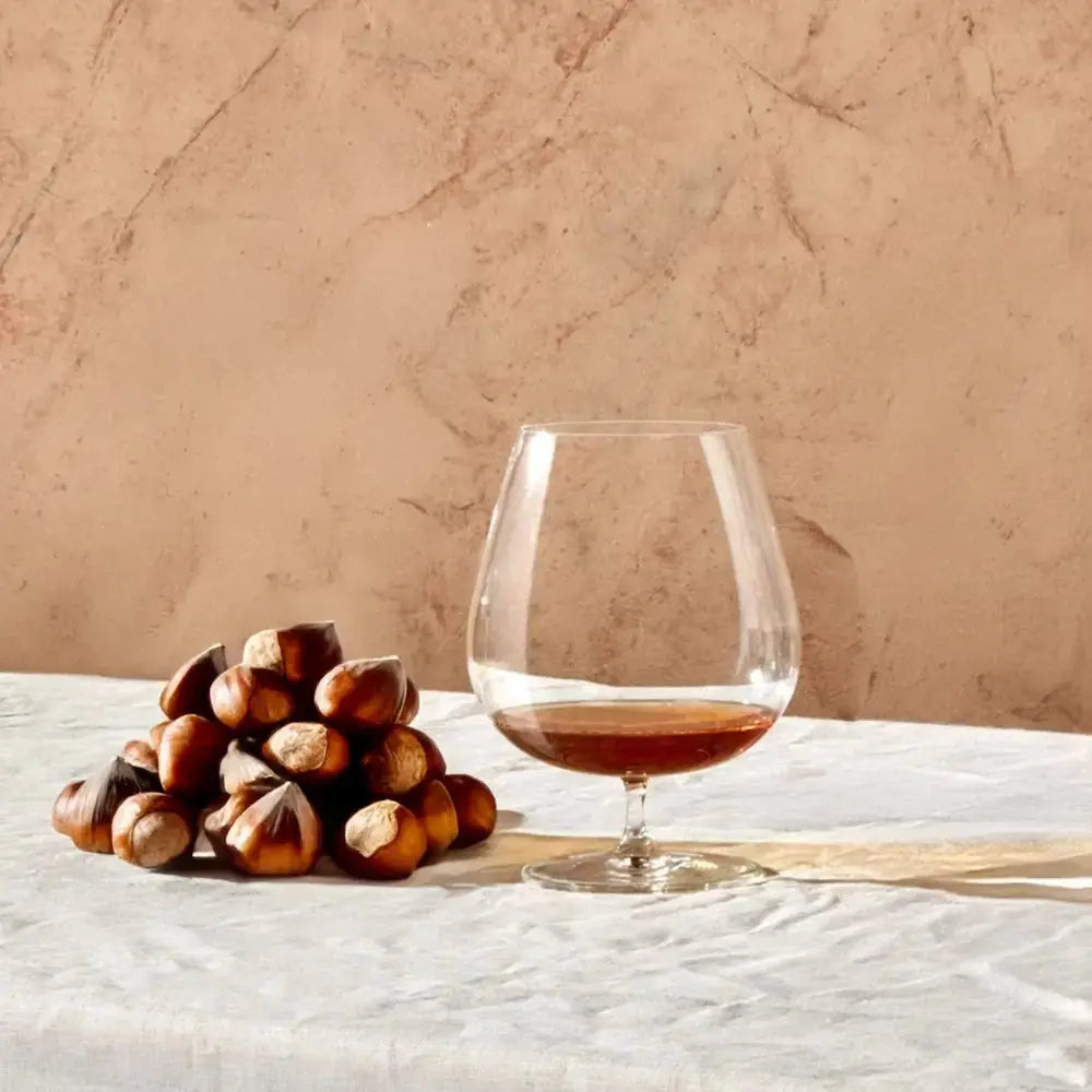 Verre à cognac ballon en cristal posé sur une table, accompagné de noisettes. Style élégant et raffiné.