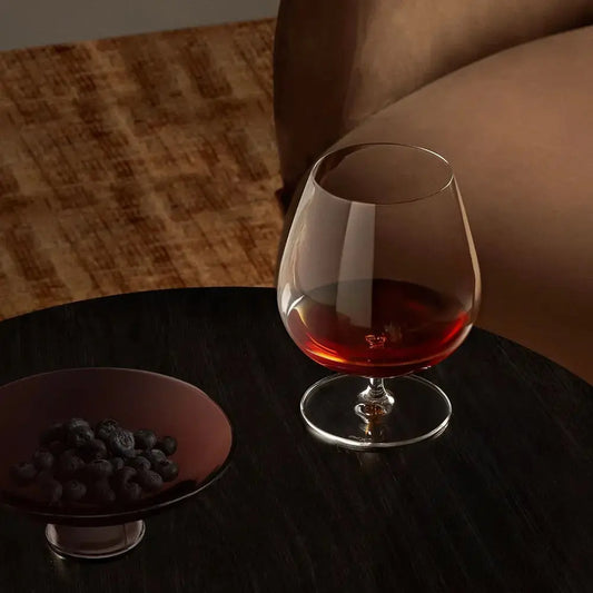 Verre à cognac ballon posé sur une table basse dans un salon cosy, ambiance lifestyle chaleureuse.