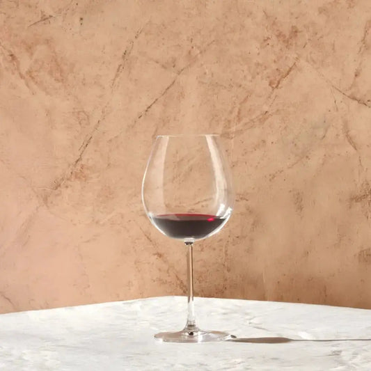 Verre à vin Bourgogne, dégustation de vin rouge sur table en marbre avec fond texturé beige.