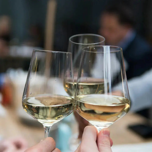 Trois verres à vin universels remplis de vin blanc portés en toast dans une ambiance conviviale au restaurant.