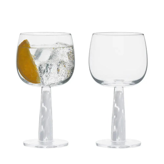 Duo de verres à gin élégants sur fond blanc, dont l’un rempli d’un gin tonic frais garni d’une tranche d’agrume et de glaçons.