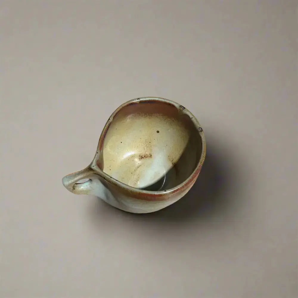 Vue de dessus d'une bolée de cidre, révélant ses nuances d'émail et sa forme unique avec anse perforée.