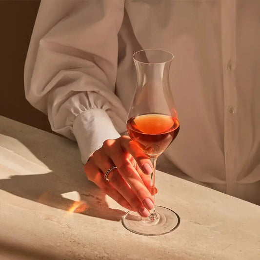 Main tenant un verre à dégustation de whisky au design raffiné, capturée dans une ambiance chaleureuse. Accessoire idéal pour amateurs de spiritueux.