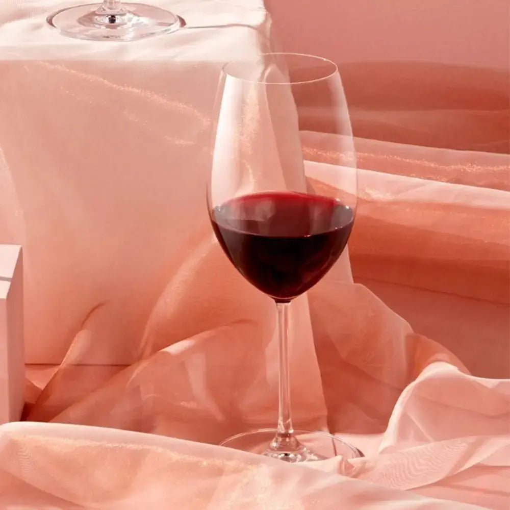 Verre à vin rouge Bordeaux posé sur un tissu élégant aux teintes rosées, capturant une ambiance raffinée et chaleureuse.