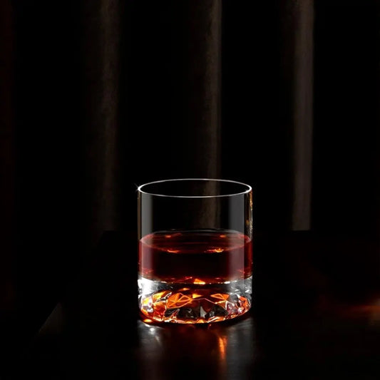 Verre à whisky effet ondulé et fond sculpté, rempli d'un spiritueux ambré. Mise en scène élégante avec éclairage tamisé et fond sombre, créant une ambiance raffinée.