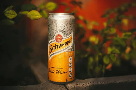 Bouteille de schweppes posée sur une table en bois. Il s'agit de la base pour le célèbre cocktail cognac schweppes.