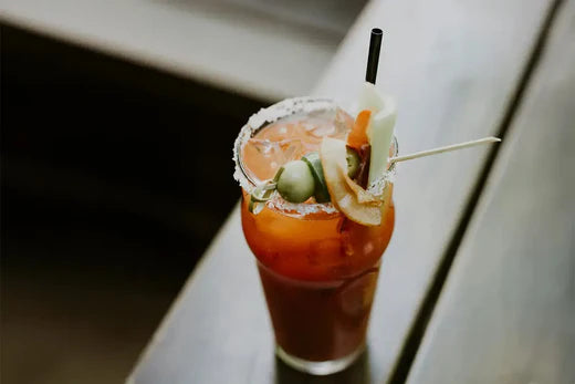 Une cocktail bloody caesar sur un table en bois. La lumière est sombre. 