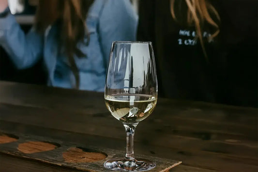 Verre INAO rempli de vin blanc. Au second plan il y a deux filles en train de discuter.