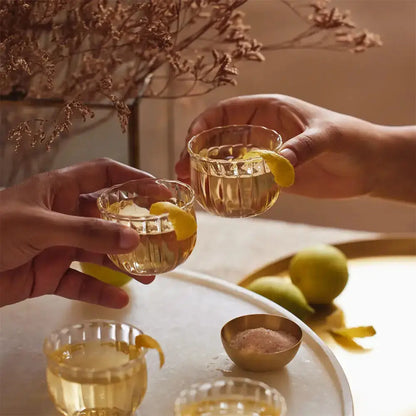 Deux personnes trinquent avec des tasses à saké. Il y a du citron et un bouquet séché en second plan.