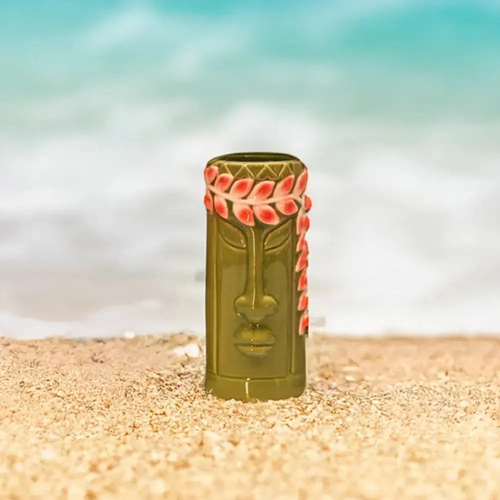 Verre tiki style hawaïenne sur une plage de sable fin et blanc. Au fond il y a la mer bleue.