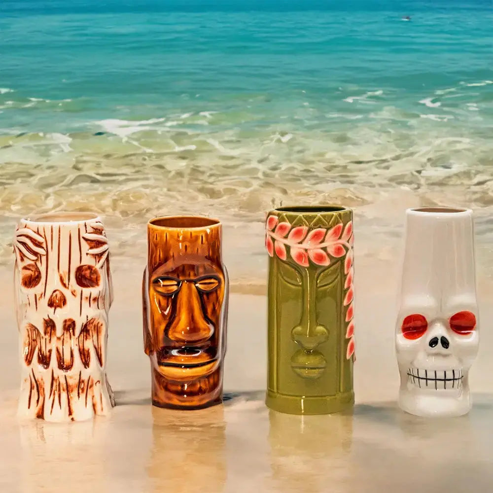 Quatre verres tiki sur du sable mouillé avec au fond l'eau de l'océan d'un plage paradisiaque. 