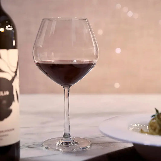 Verre à Bourgogne rempli de vin rouge sur une table en marbre. Il y a une bouteille de vin rouge à côté.