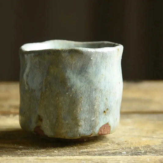 Verre à saké en céramique sur une table en bois.