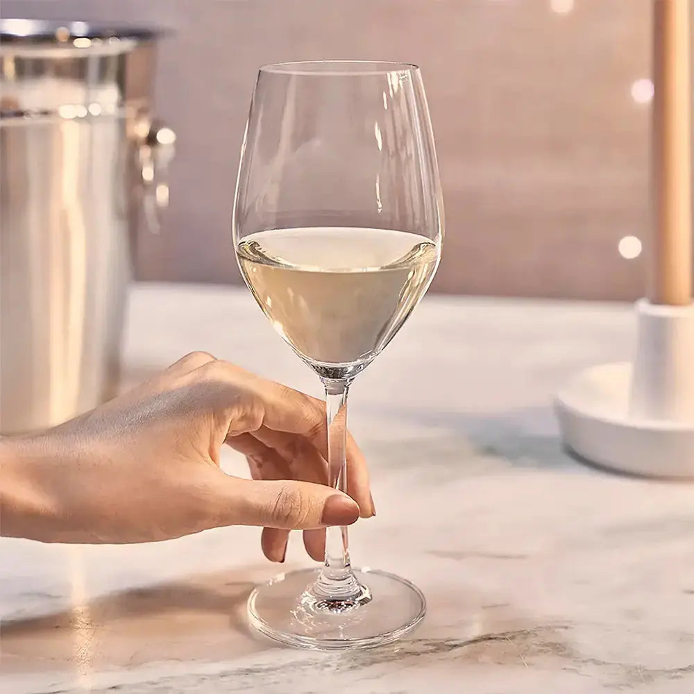 Verre pour vin blanc rempli de vin blanc. Une femme tiens le verre du bout des doigts. Au fond il y a un seau en aluminium.