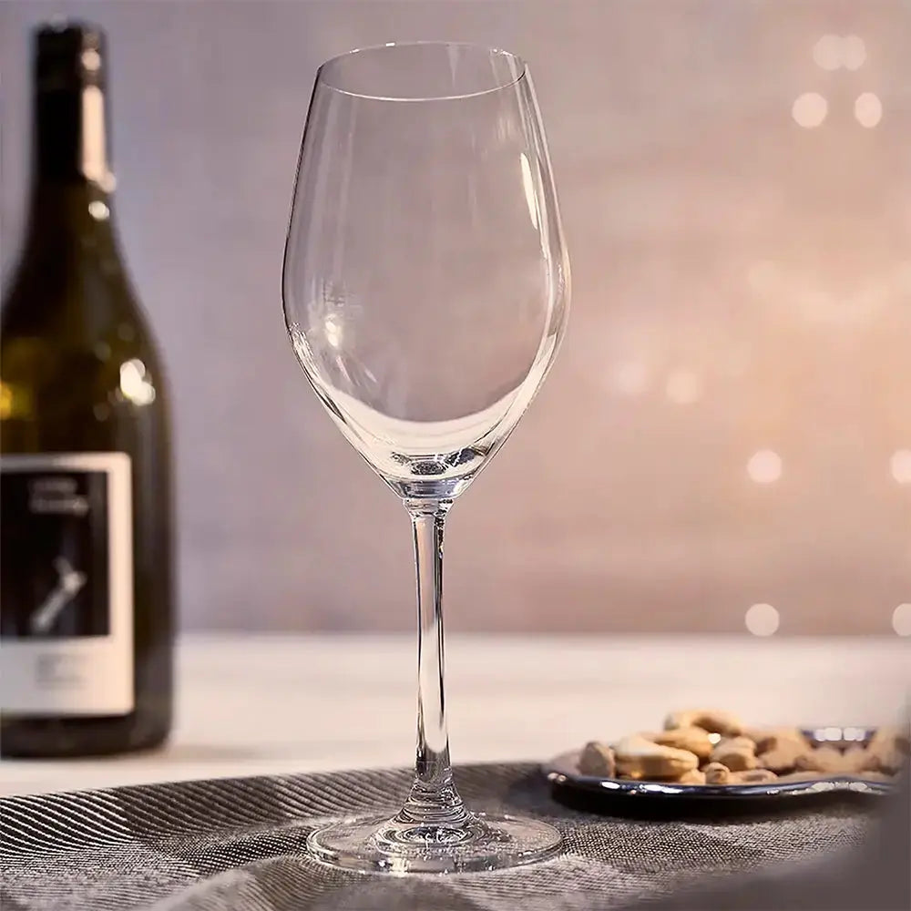 Verre pour vin blanc vide. Il y a des cacahuètes a côté et une bouteille de vin blanc ouverte sur la gauche. 