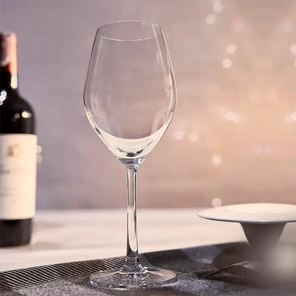 Verre pour vin rouge vide posé sur la nappe d'une table blanche. Derrière il y a une bouteille de vin rouge.