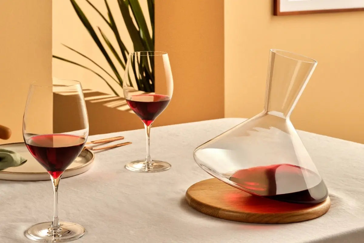 Carafe à vin remplie de vin posée sur une table. Il y a deux verres de vin pleins à côté. Ces accessoires de vin sont sur une nappe blanche.