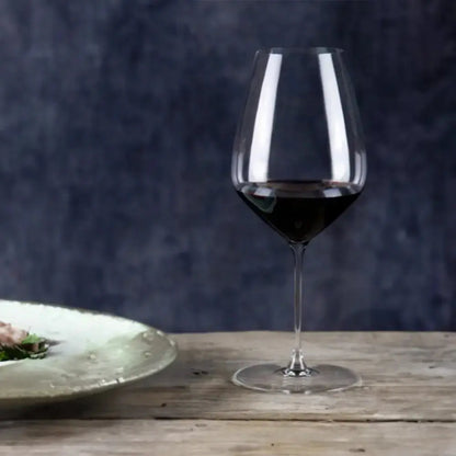 Un verre à vin rouge original sur une table en bois. Il y a une assiette de nourriture sur la gauche et le fond et de couleur violet.