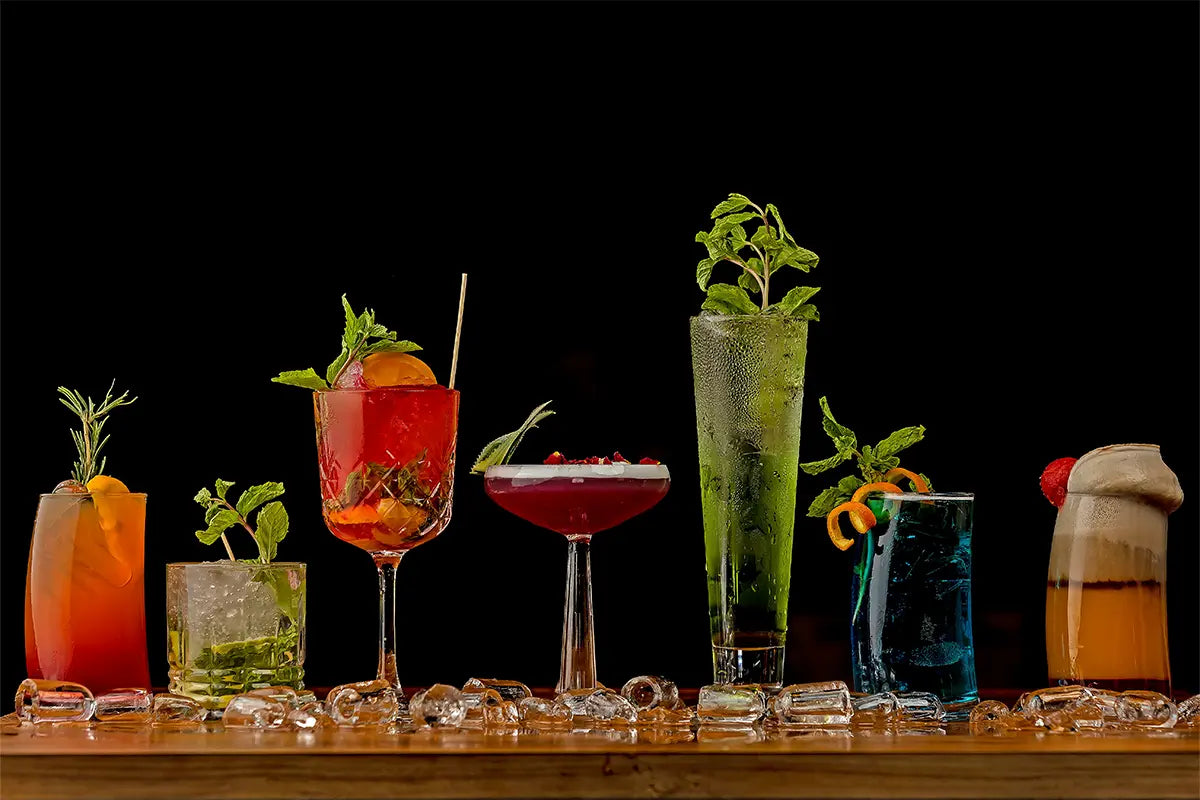 Ensemble de différents verres pour cocktails et spiritueux sur une table en bois avec un fond noir.